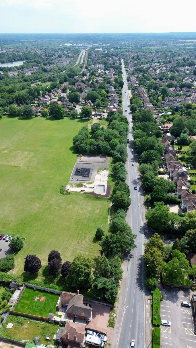 Aerial view of a suburban area with green fields and roads lined with houses.