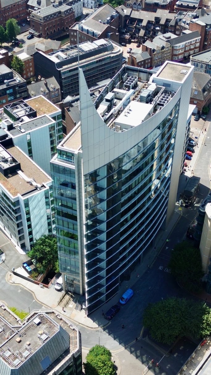 Modern skyscraper with a pointed rooftop and glass exterior in an urban setting.