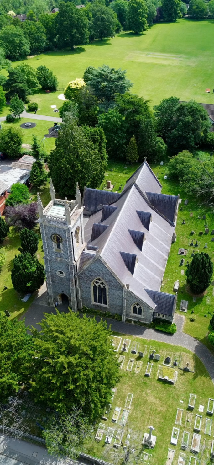 Aerial view of a stone church surrounded by trees and a graveyard.