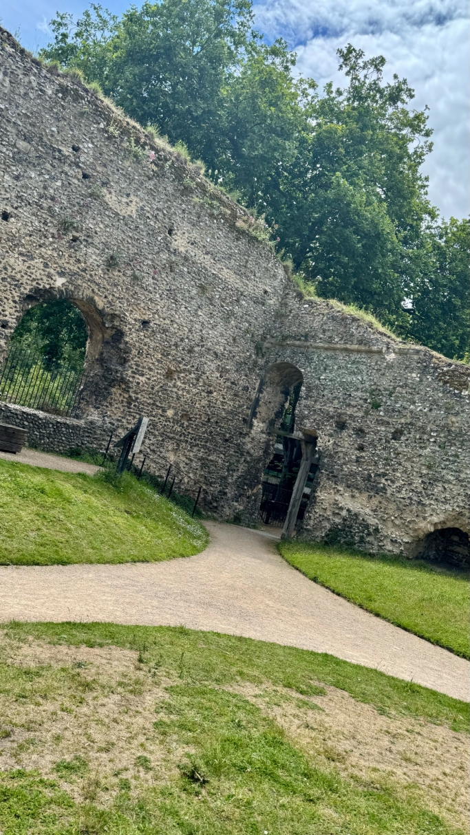 Ruined stone wall with a pathway and greenery in a historical site.