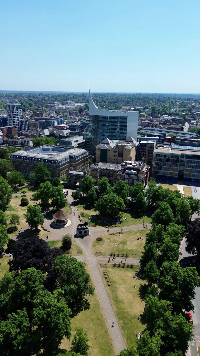 Aerial view of a city park surrounded by buildings and greenery on a sunny day.