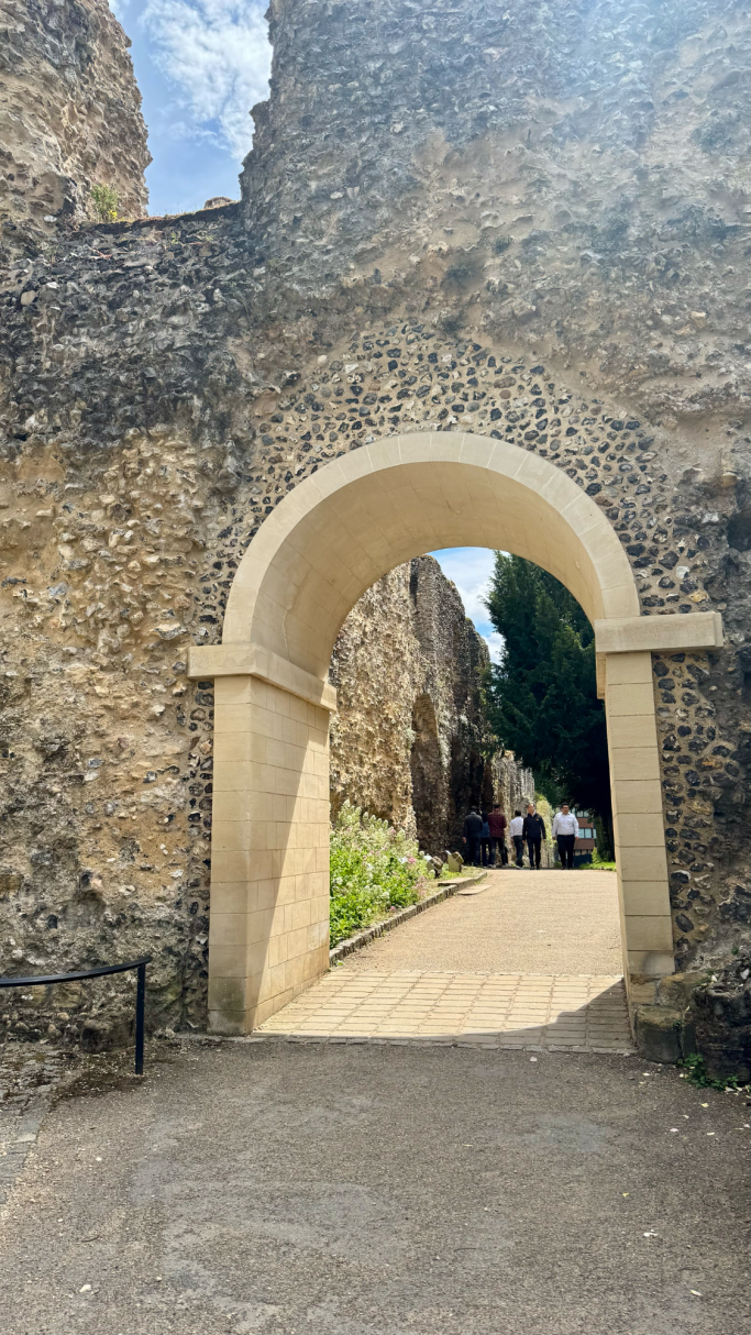 Stone archway leading to a pathway flanked by ancient walls and greenery.