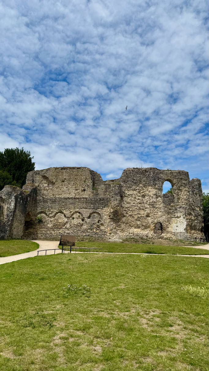 Stone ruins of a historical structure against a blue sky and grassy area.