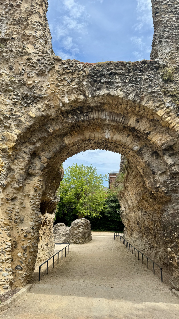 Stone archway in historical ruins, leading to a grassy area with trees.