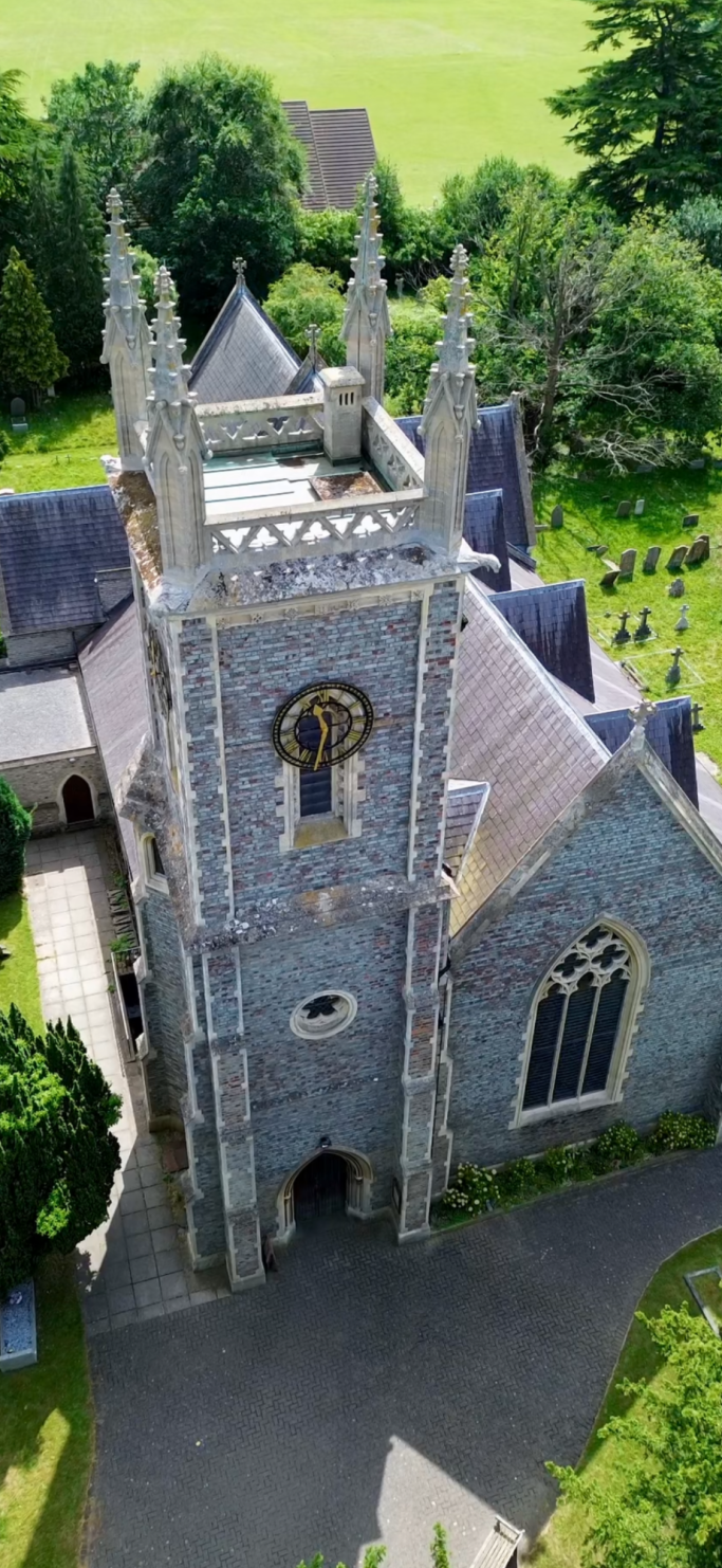 Stone church with a tower, surrounded by greenery and a graveyard.